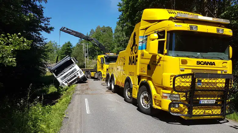 En lastebil med kran som lufter en lastebil opp på veien igjen